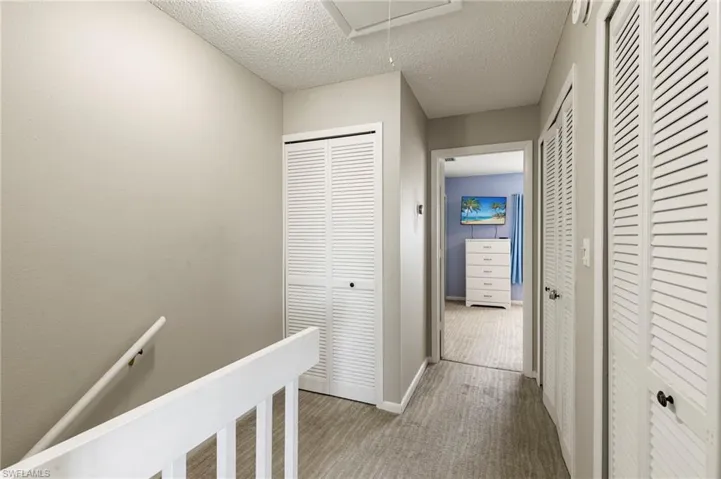 Corridor with an upstairs landing, attic access, and light colored carpet