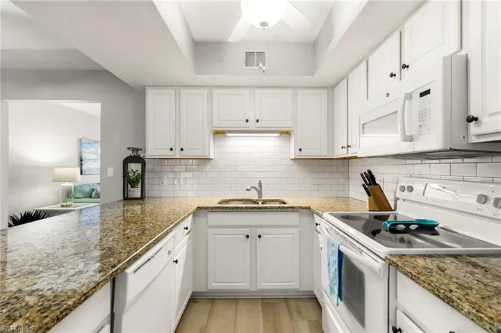 Kitchen featuring white appliances, dark stone countertops, white cabinetry, and decorative backsplash
