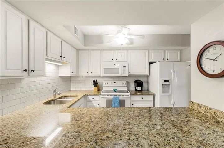 Kitchen with white cabinets, white appliances, backsplash, and light stone countertops