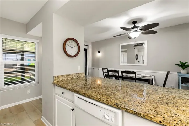 Kitchen featuring dark stone countertops, white dishwasher, white cabinets, light wood-type flooring, and a ceiling fan