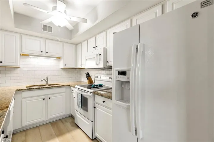 Kitchen with white appliances, decorative backsplash, white cabinets, and light stone countertops