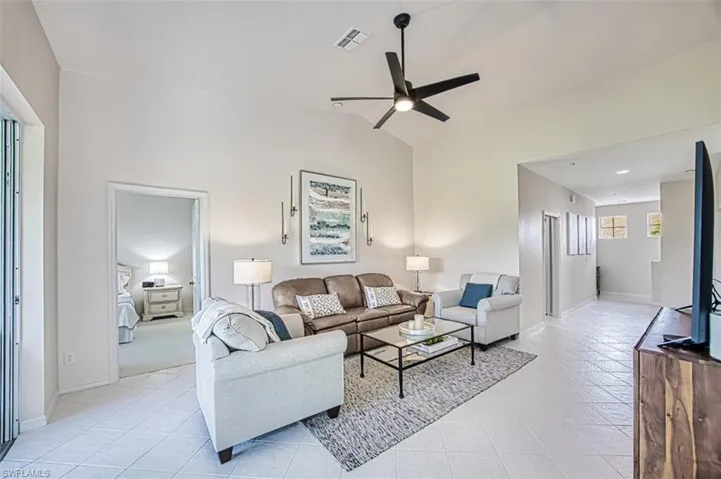 Living area with vaulted ceiling, light tile patterned flooring, visible vents, and ceiling fan