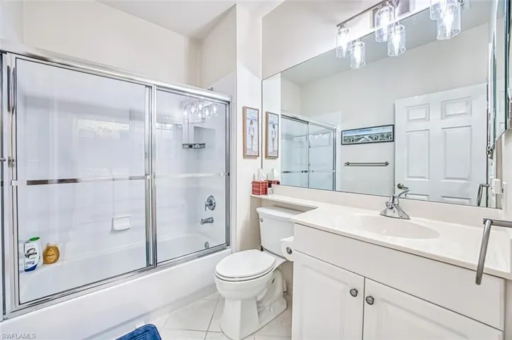 Bathroom featuring tile patterned flooring, toilet, vanity, and enclosed tub / shower combo