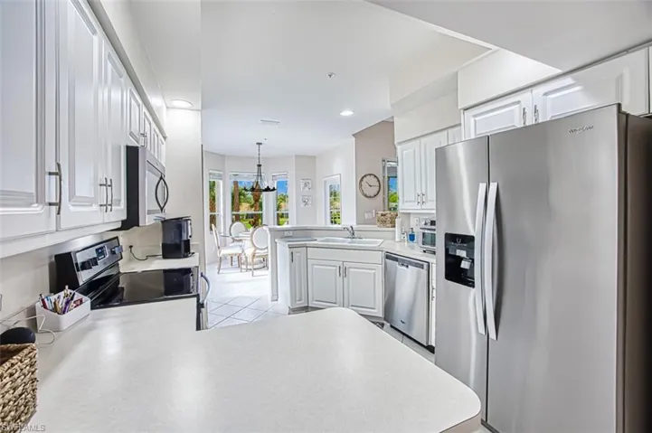 Kitchen with a peninsula, a sink, stainless steel appliances, light countertops, and a notable chandelier