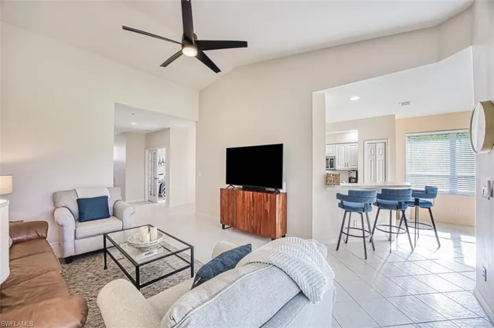 Living room with lofted ceiling, light tile patterned flooring, a ceiling fan, and baseboards