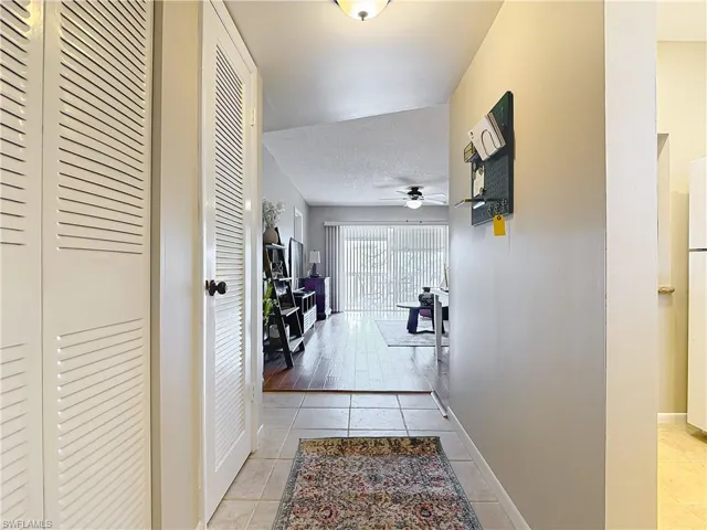 Hallway with light tile patterned floors, baseboards, and a textured ceiling