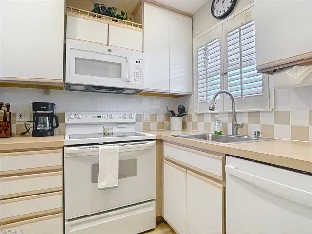 Kitchen featuring white appliances, a sink, tasteful backsplash, light countertops, and white cabinets