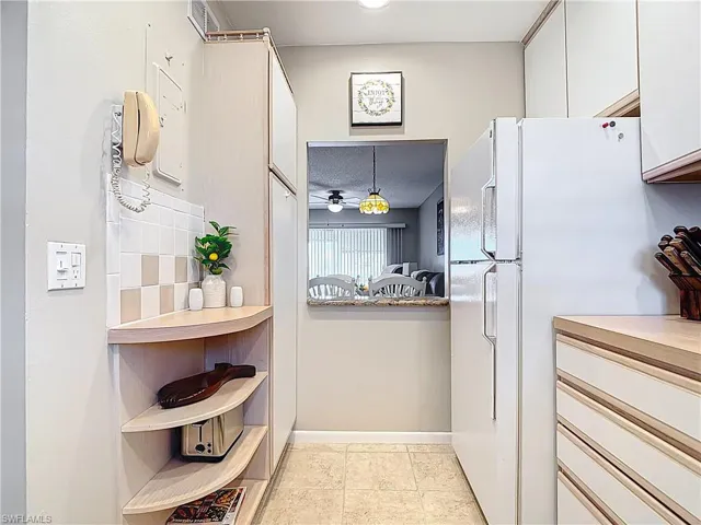 Kitchen with freestanding refrigerator, white cabinets, open shelves, backsplash, and light countertops