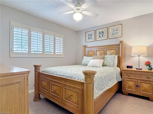 Bedroom with light colored carpet, multiple windows, a ceiling fan, and a textured ceiling