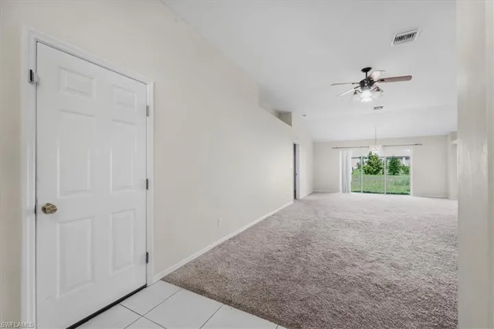 Spacious living area featuring neutral carpeting, a ceiling fan with integrated lighting, and vaulted ceilings
