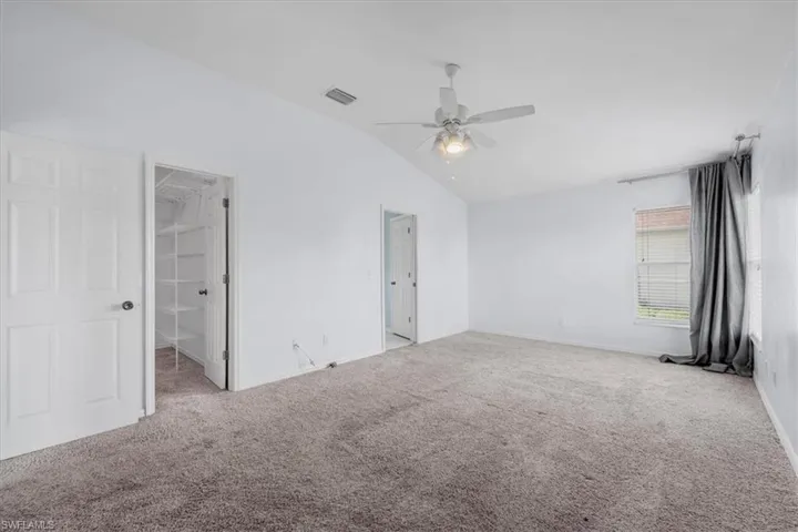 Spacious room featuring vaulted ceilings, textured carpet flooring, a ceiling fan with light fixture, and a window with horizontal blinds
