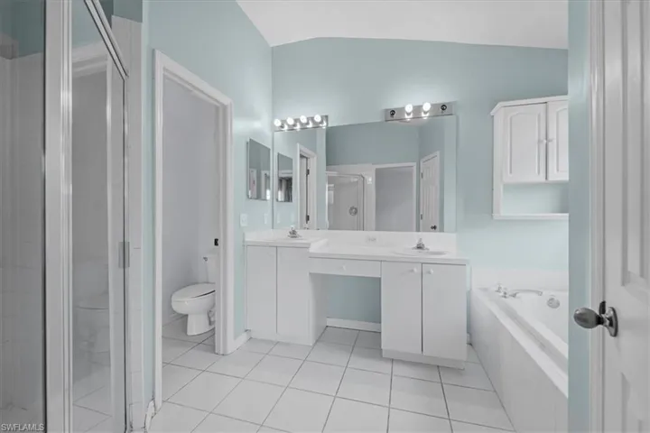 Bathroom featuring a dual vanity, built-in cabinetry, large mirror with vanity lighting, tiled flooring, and a garden tub