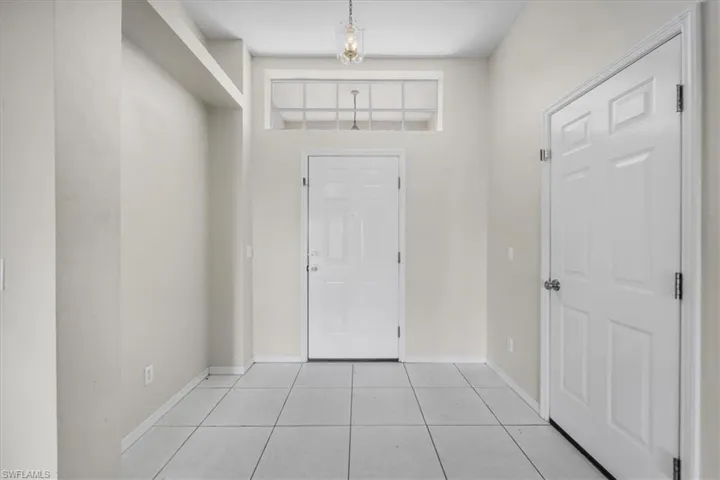 Entryway featuring a panel door with transom window, tile flooring, recessed architectural detailing, and a pendant light fixture