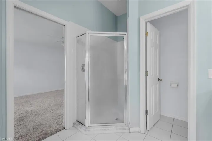Glass-enclosed corner shower with white subway tile interior, set on a white tiled floor