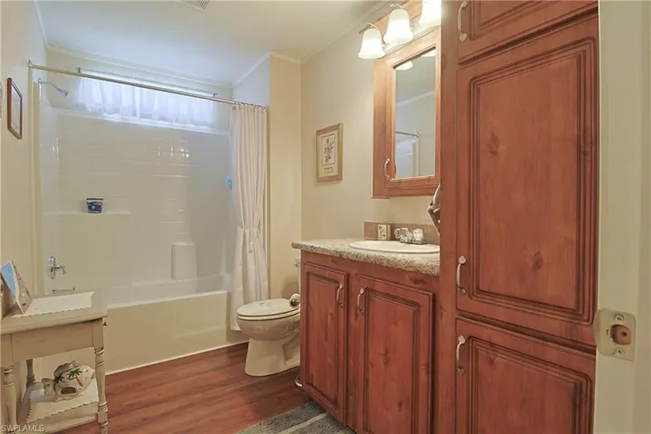 Bathroom with vanity, dark wood-type flooring, ornamental molding, and shower / tub combo with curtain