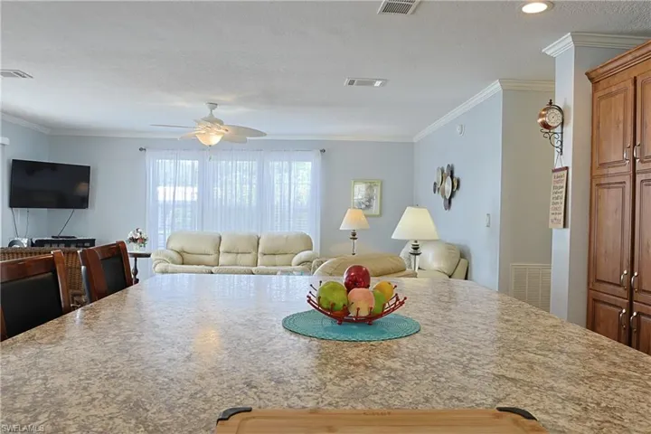Kitchen featuring open floor plan, crown molding, a textured ceiling, a ceiling fan, and light stone countertops