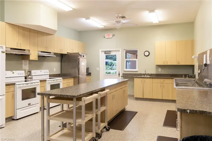 Kitchen with light wood finish cabinetry, white appliances, dark countertops, ceiling fan, and a center island