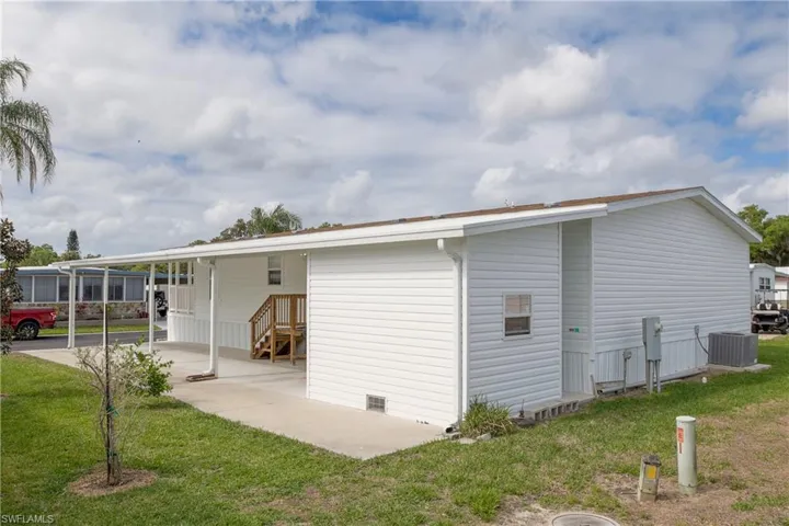Rear view of property with a lawn, an attached carport, and covered porch