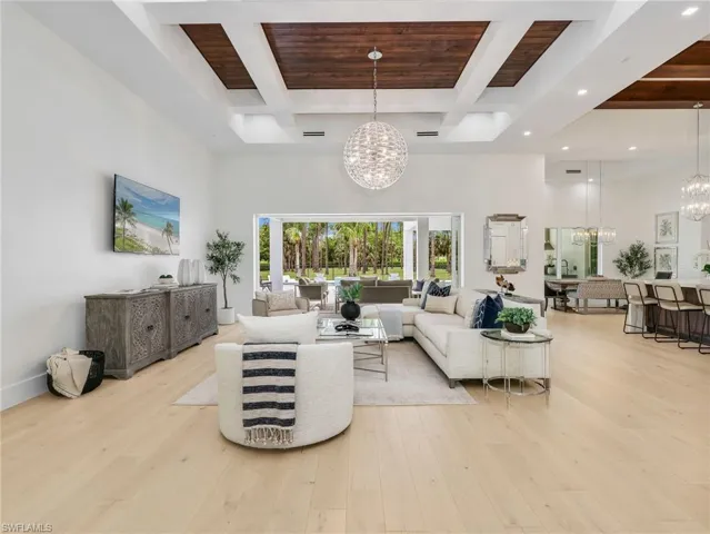 Open concept living area w/ Coffered ceiling, wood-finish inserts, recessed lighting, and a crystal chandelier