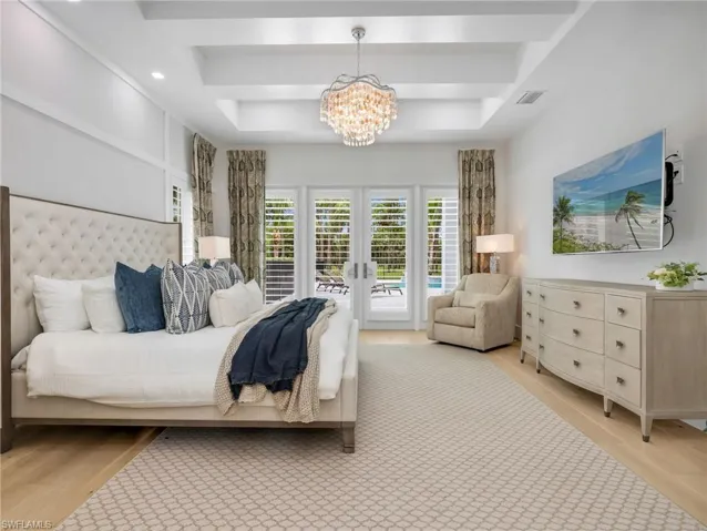 Tray ceiling with a chandelier, light wood flooring, white plantation shutters, and double French doors to an outdoor area