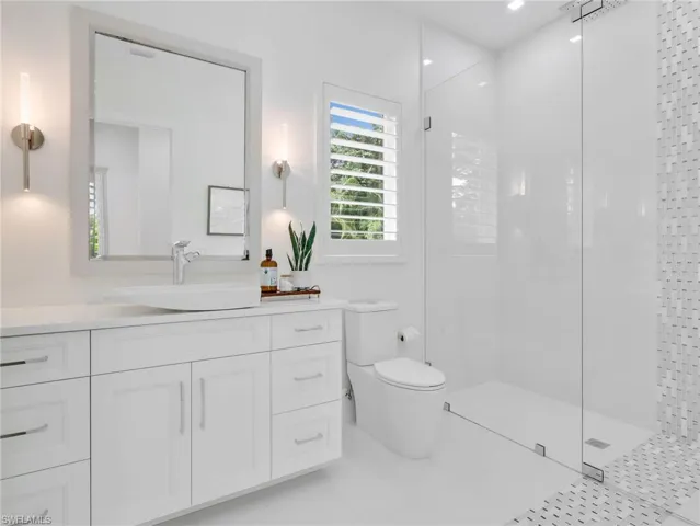 White shaker-style vanity with a vessel sink, a walk-in shower with clear glass enclosure, a rainfall shower head, and a mosaic tile accent wall. This bathroom serves the bonus room and pool area
