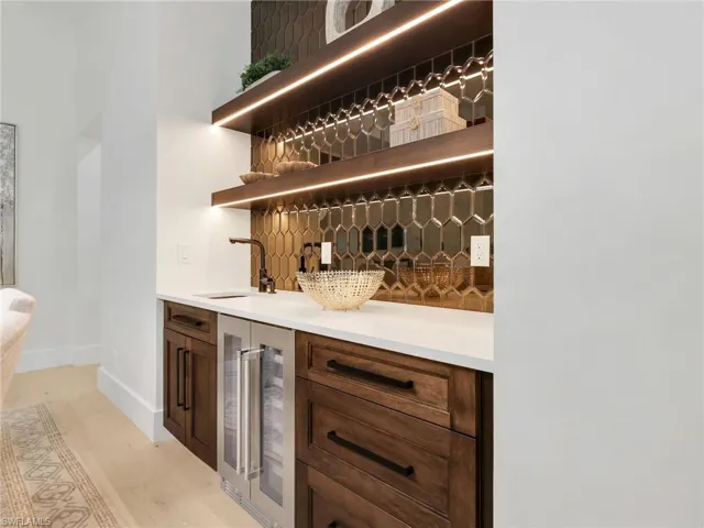 Built-in wet bar featuring wood cabinetry, white countertop, integrated beverage cooler, and a tiled backsplash
