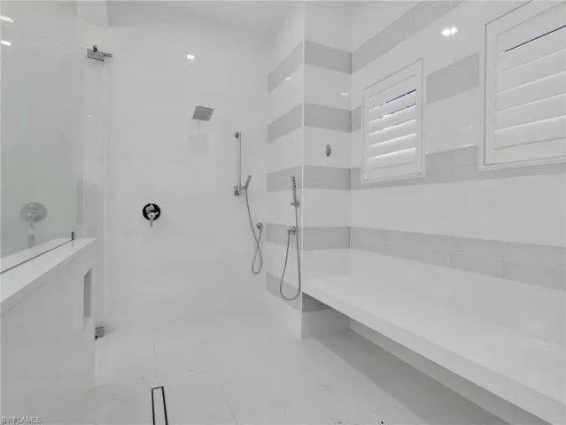 Spacious shower featuring a glass enclosure, rainfall showerhead, handheld shower fixture, built-in bench, and plantation shutters