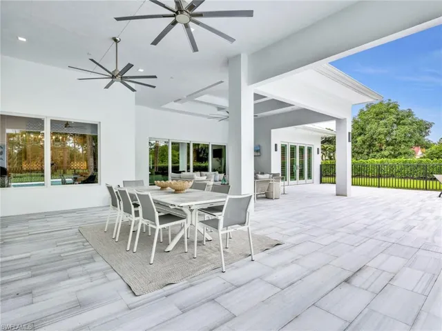 Expansive covered patio featuring a light-toned tile floor, multiple ceiling fans, and large windows