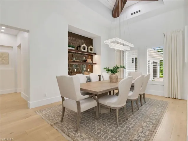 Vaulted ceiling with exposed wood beams, built-in wet bar w/ display shelving and integrated lighting, and multiple windows with Custom-crafted plantation shutters with oversized wood louvers