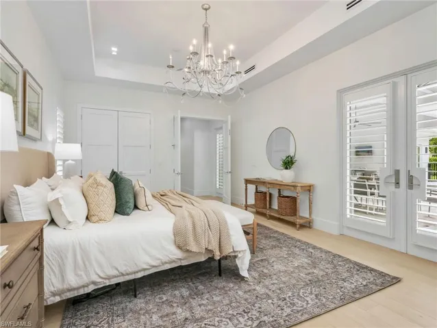 Off pool area and could be used for a bonus room. Tray ceiling with a chandelier, wood-finish flooring, and white double doors with louvered panels