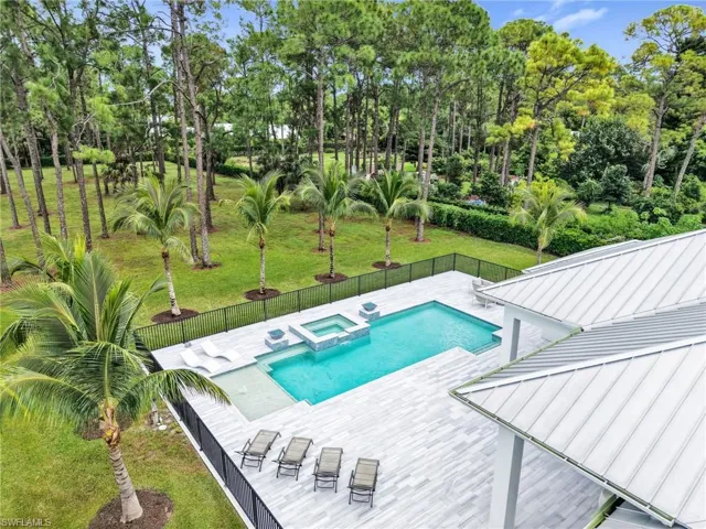 Expansive outdoor living area featuring a rectangular pool and integrated spa, surrounded by a light-toned paved deck