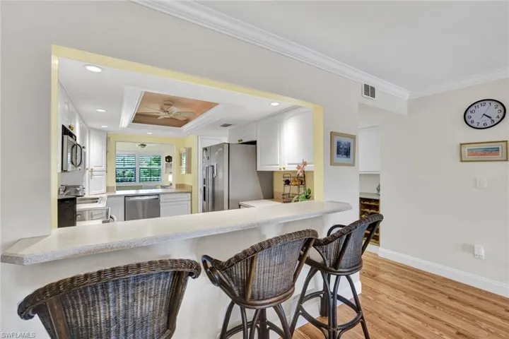 Kitchen featuring crown molding, white cabinets, a breakfast bar area, light wood-style floors, and light countertops