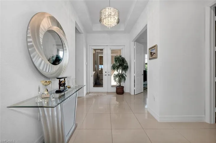 Entrance foyer with a notable chandelier, light tile patterned floors, a tray ceiling, and french doors
