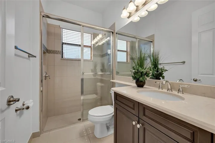 Bathroom with toilet, vanity, tile patterned floors, and a shower with shower door