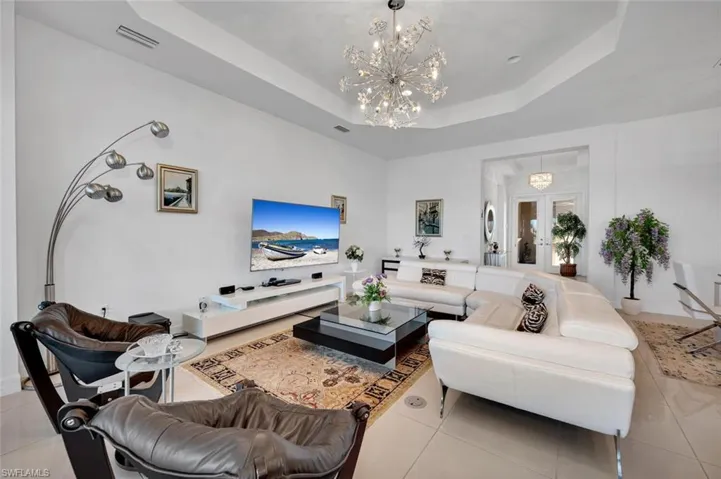 Tiled living room featuring a chandelier, french doors, and a raised ceiling