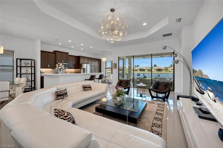 Living room with light tile patterned floors, an inviting chandelier, a raised ceiling, and a water view