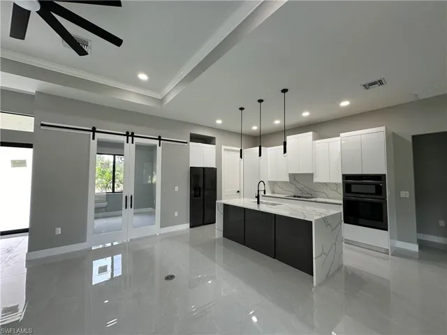 Kitchen with a barn door, ceiling fan, white cabinets, and a kitchen island with sink
