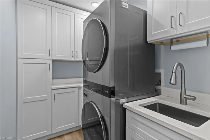 Clothes washing area with cabinets, light hardwood / wood-style floors, stacked washer and clothes dryer, and sink