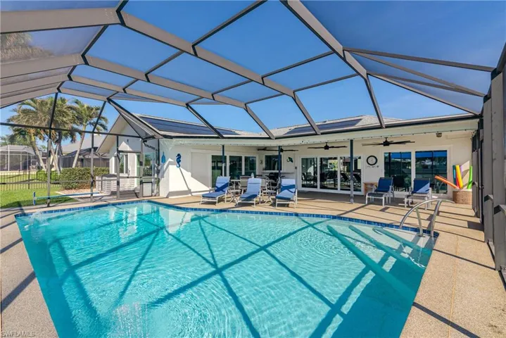 View of swimming pool featuring glass enclosure, ceiling fan, and a patio area