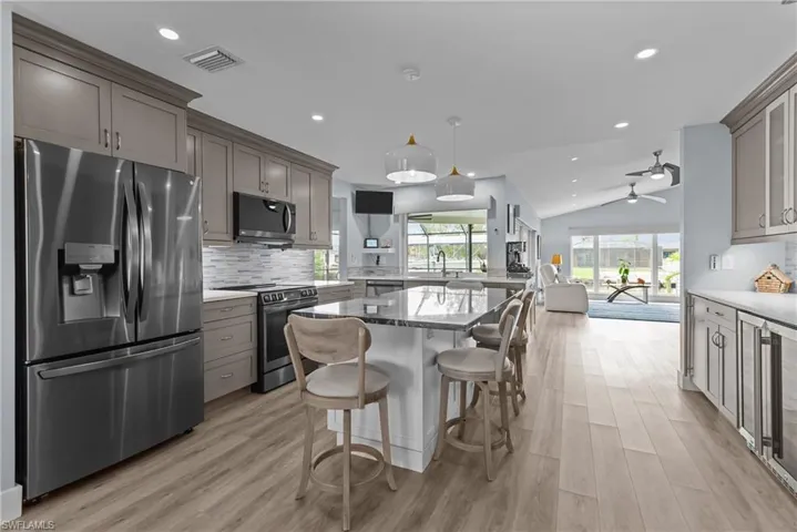 Kitchen with hanging light fixtures, stainless steel appliances, light stone counters, light hardwood / wood-style floors, and vaulted ceiling
