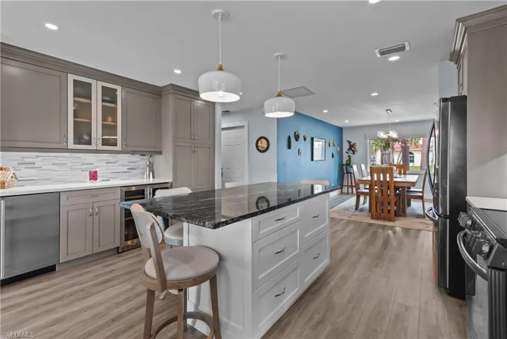 Kitchen with beverage cooler, hanging light fixtures, light hardwood / wood-style floors, gray cabinets, and appliances with stainless steel finishes