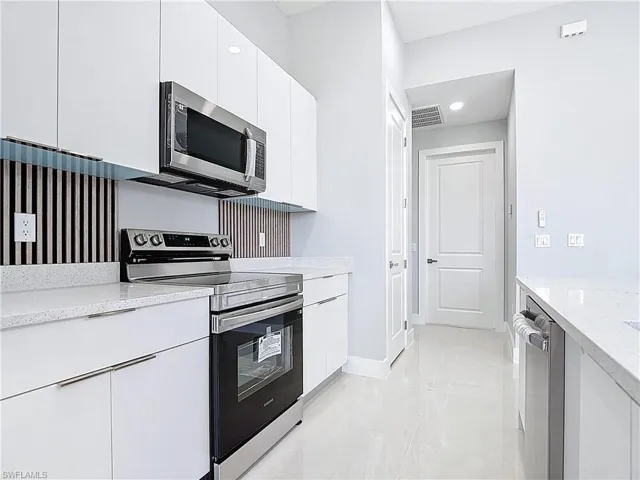 Kitchen with stainless steel appliances, white cabinetry, light stone counters, and modern cabinets