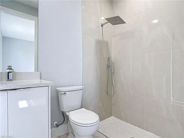 Full bath featuring a textured wall, vanity, and tiled shower
