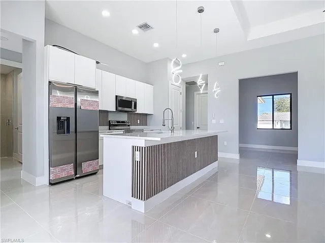 Kitchen featuring white cabinetry, stainless steel appliances, a kitchen island with sink, decorative light fixtures, and light stone counters