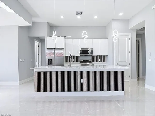 Kitchen featuring white cabinetry, a large island, stainless steel appliances, and decorative light fixtures