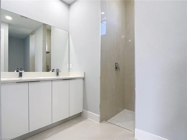 Full bathroom featuring a walk in shower, double vanity, a textured wall, and light tile patterned flooring
