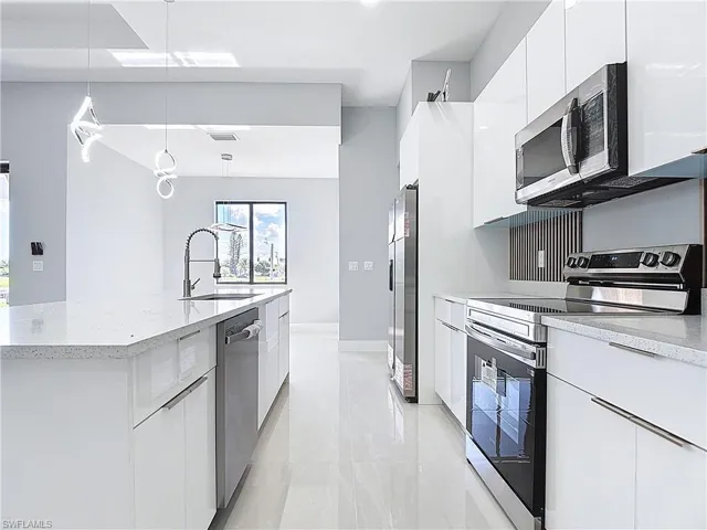 Kitchen with stainless steel appliances, white cabinets, decorative light fixtures, a kitchen island with sink, and modern cabinets