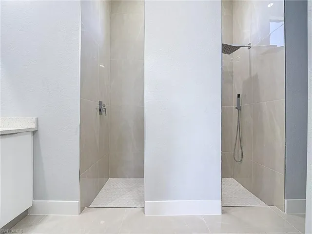 Bathroom featuring a walk in shower, vanity, a textured wall, and light tile patterned floors