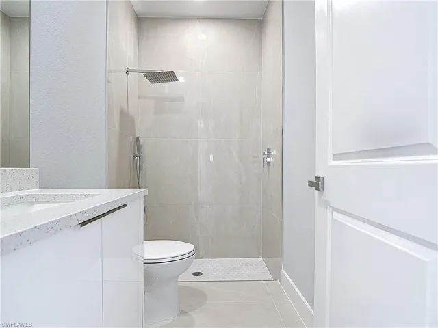 Full bath featuring tiled shower, a textured wall, and vanity