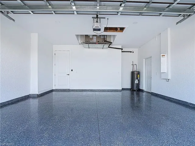 Garage with water heater, electric panel, and a textured wall